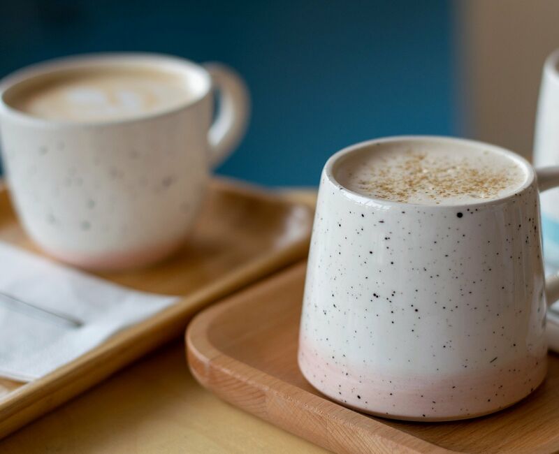 Zwei Keramiktassen mit Kaffee auf Holztabletts, eine mit Schaum und Gewürzen. Bilddatei: dummy.jpg.