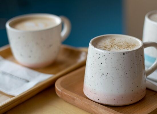 Zwei Keramiktassen mit Kaffee auf Holztabletts, eine mit Schaum und Gewürzen. Bilddatei: dummy.jpg.